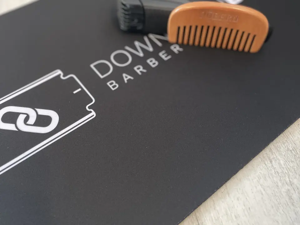 Fekete céges egérpad fehér Downtown Barber logóval, fésűvel a felületén